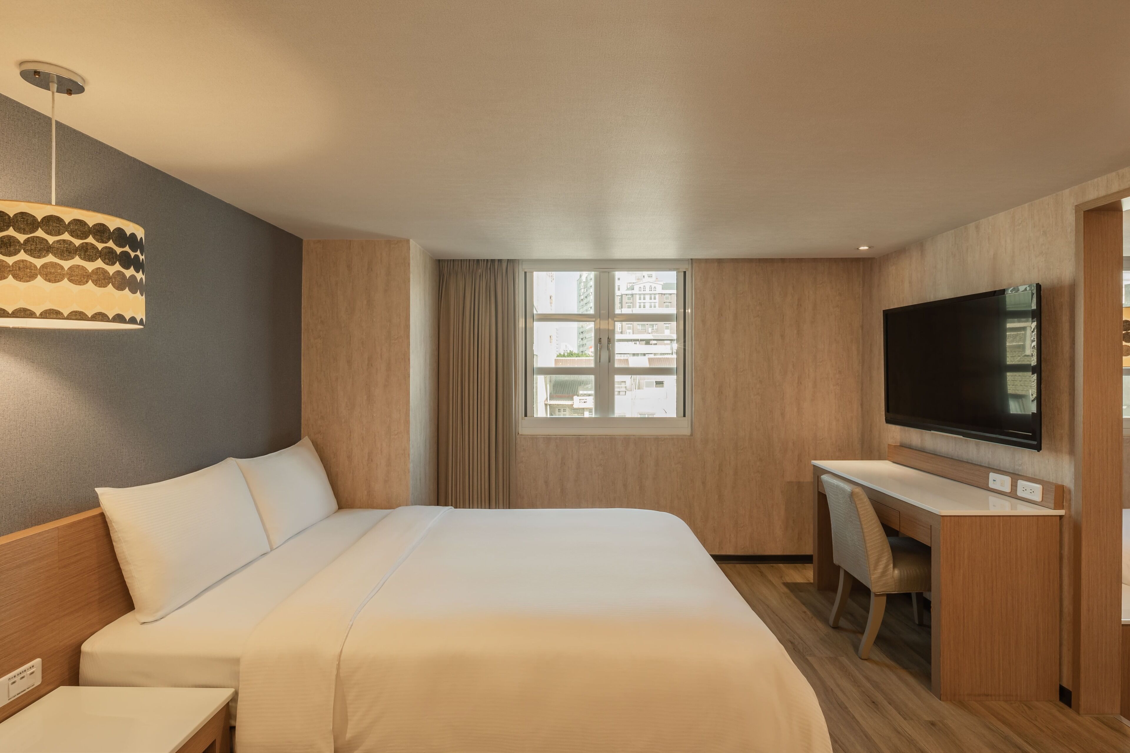 A hotel room with a bed, a desk, a television, and a window with curtains.