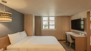 A hotel room with a bed, a desk, a television, and a window with curtains.