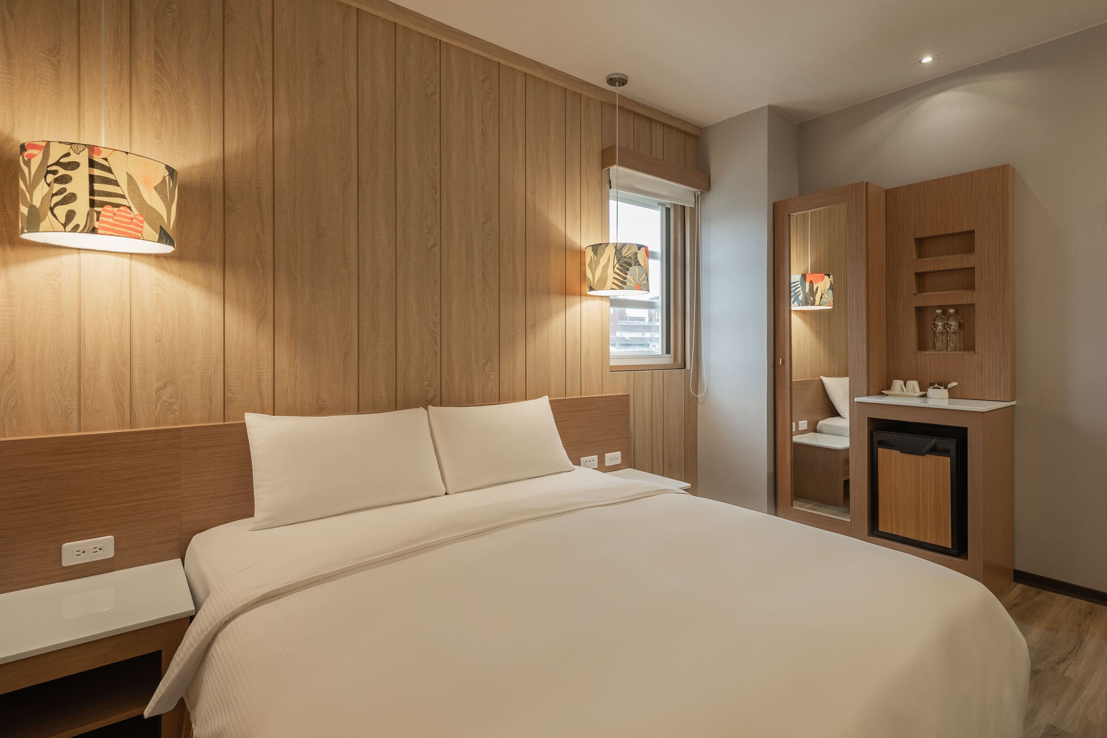 Un dormitorio moderno con cabecera de madera, cama con sábanas blancas, mesita de noche, armario empotrado y ventana con persianas.