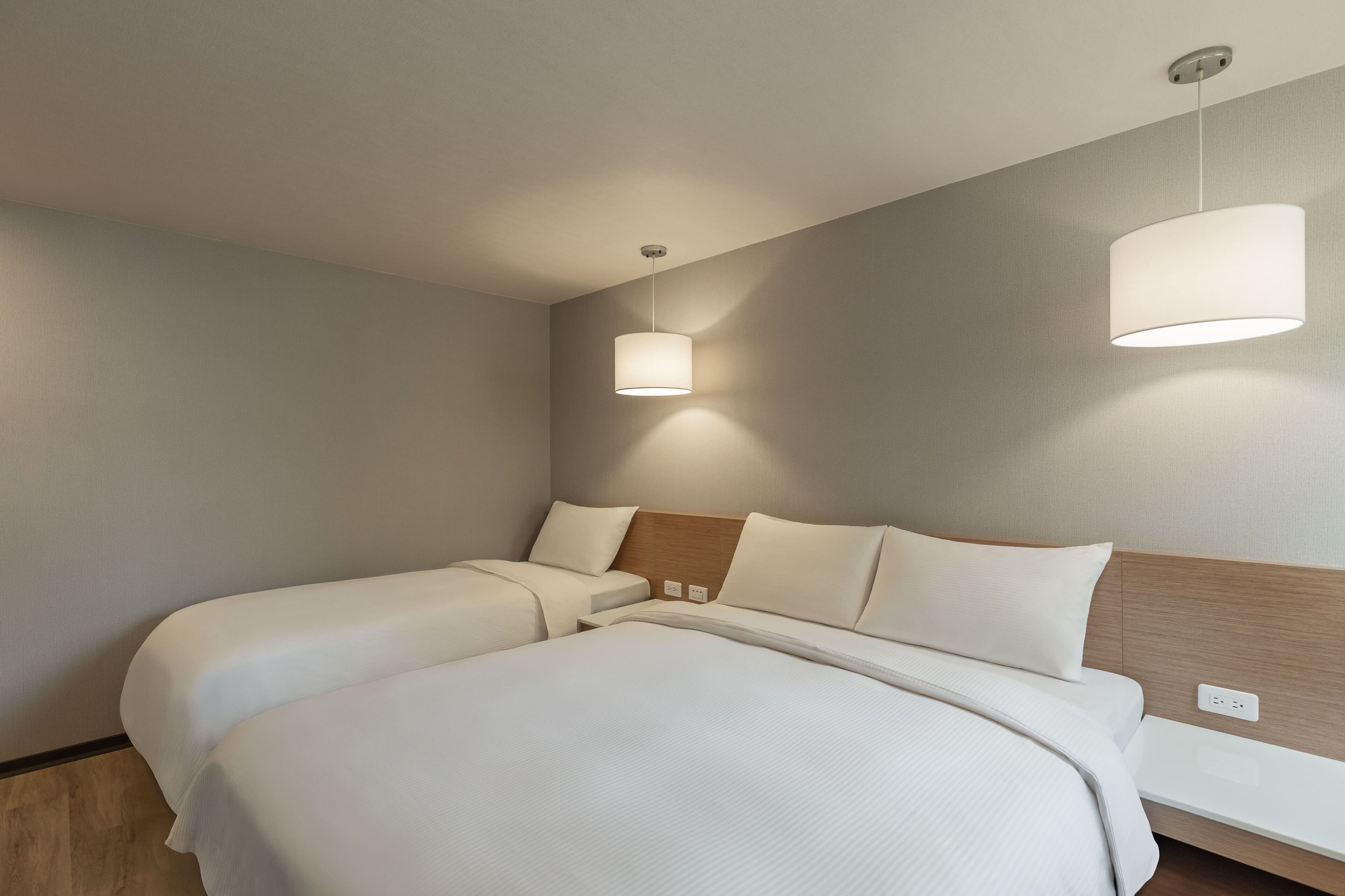Una habitación de hotel moderna con dos camas, cabecero de madera y una lámpara en el techo.
