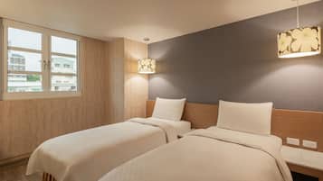 A hotel room with two beds, a window, a wall-mounted lamp, and a wooden headboard.