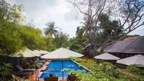 A pool area with lounge chairs and umbrellas, surrounded by lush greenery and trees. - La Mer Resort (Phu Quoc)