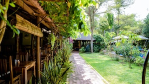 A pathway leading to a wooden structure with tables and chairs, surrounded by lush greenery and a well-maintained lawn. - La Mer Resort (Phu Quoc)