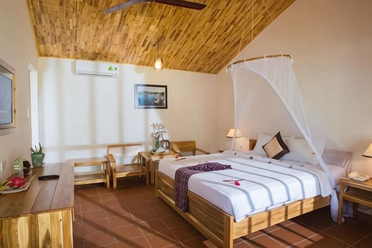 A bedroom with a wooden ceiling, a bed with a canopy, a desk, and a chair.