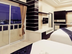 A modern hotel room with a large bed, a TV, a minibar, and a view of the city at night.