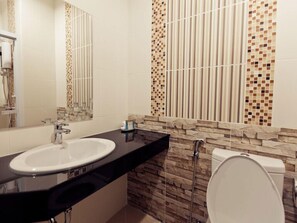 A bathroom with a white sink, a mirror, a toilet, and a shower with mosaic tiles. - Excella Hotel (Ubon Ratchathani)