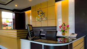 A hotel reception desk with a laptop, a phone, and a vase of flowers. - Excella Hotel (Ubon Ratchathani)