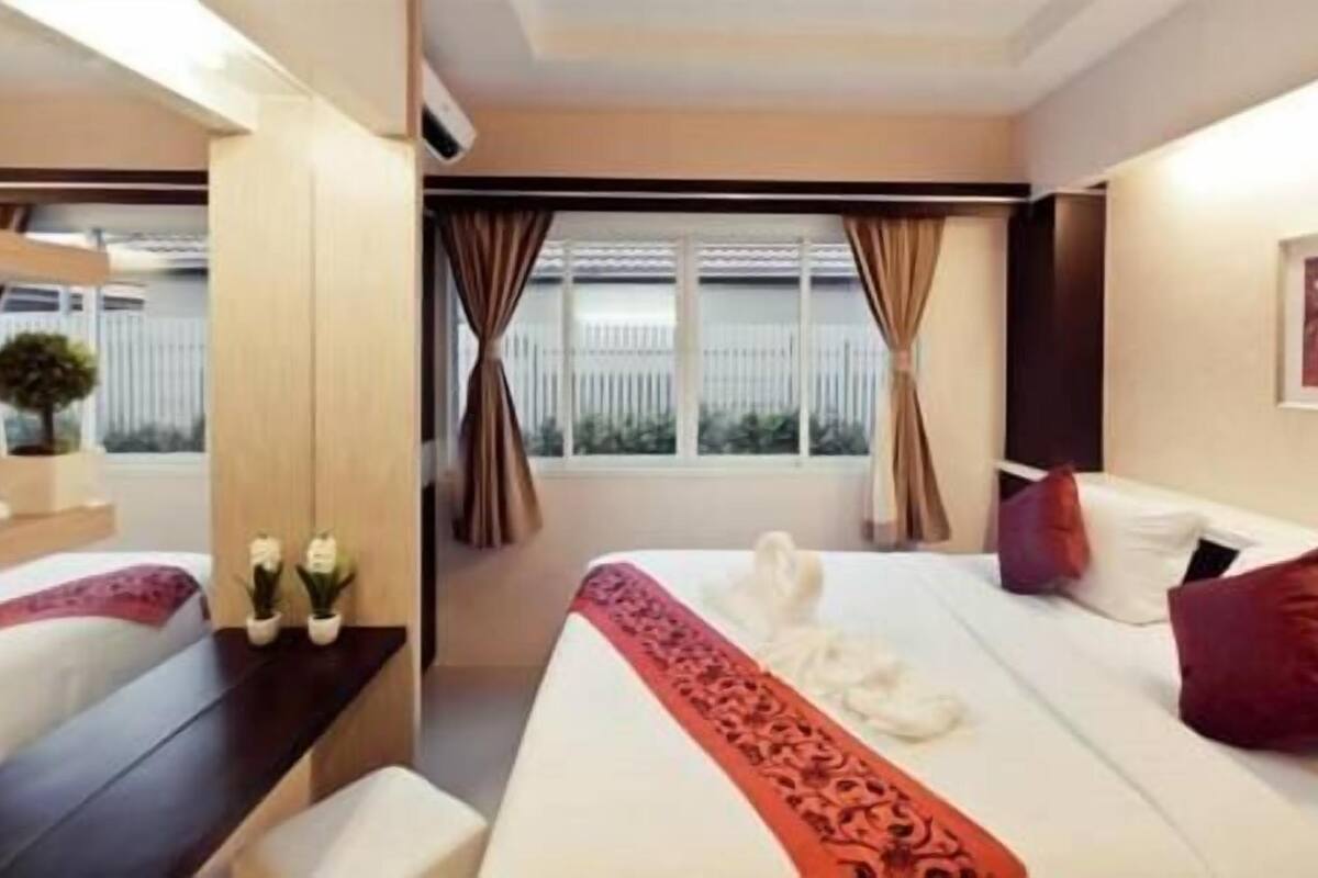 Habitación de hotel con cama, escritorio, silla, ventana con cortinas y una planta pequeña.