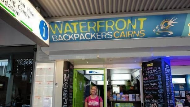 Albergue chamado 'Waterfront Backpackers Cairns' com uma porta verde e uma placa anunciando ofertas.