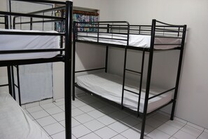 Habitación con literas, ropa de cama blanca y suelo de baldosas.