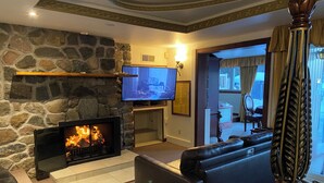 Una sala de estar con chimenea de piedra, un sofá de cuero negro, un televisor de pantalla plana y un espejo grande.