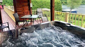 Un jacuzzi en una terraza de madera con vistas a un lago y un bosque.