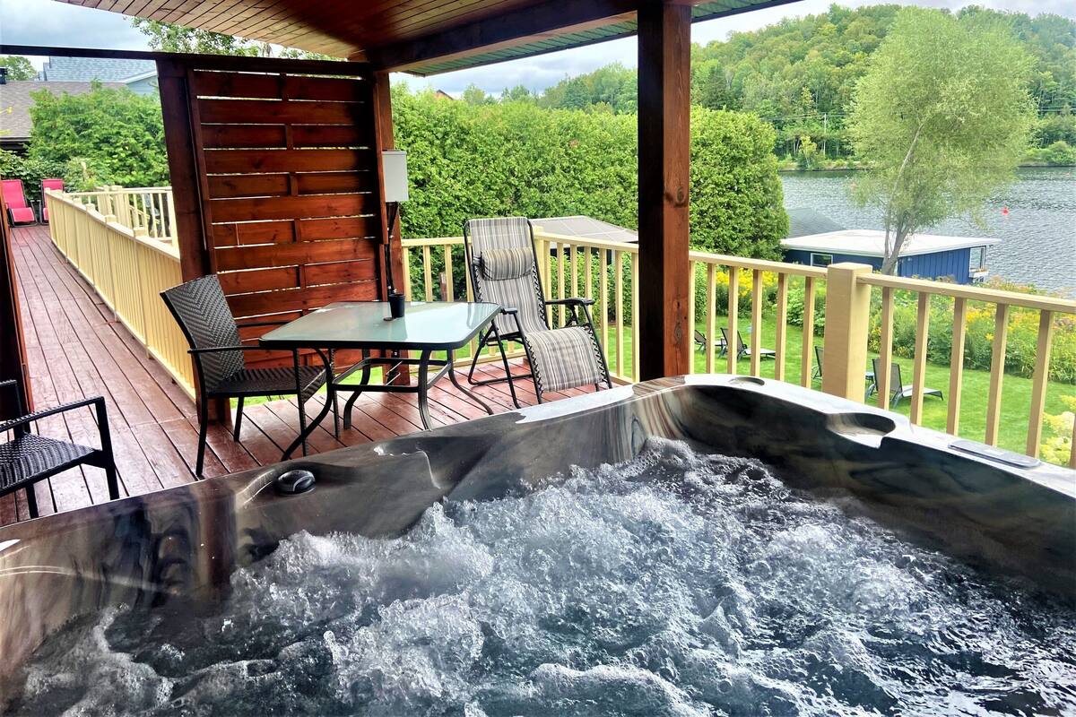 Un jacuzzi en una terraza de madera con vistas a un lago y un bosque.