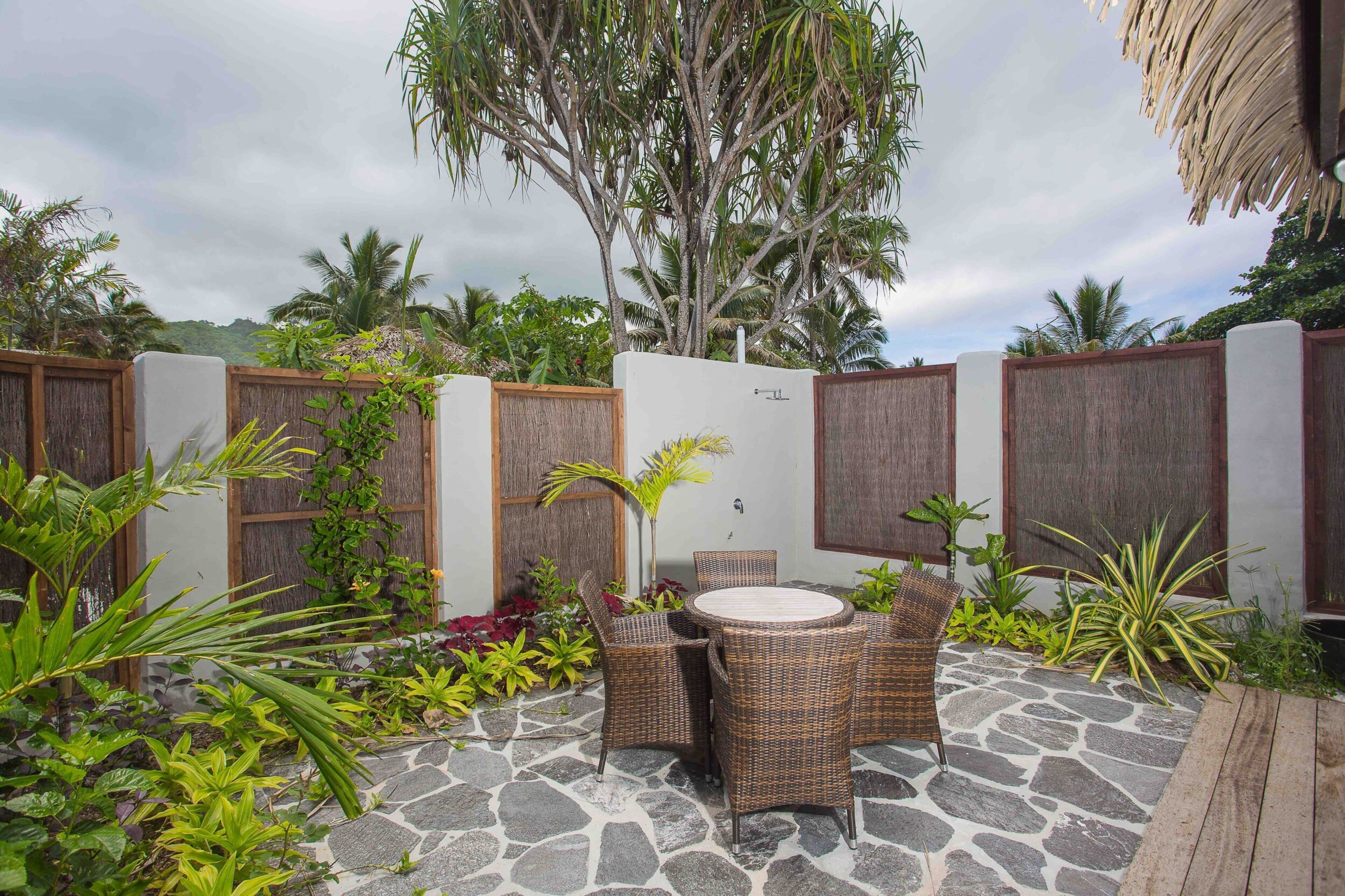 An outdoor patio with stone flooring, wicker furniture, and tropical plants.
