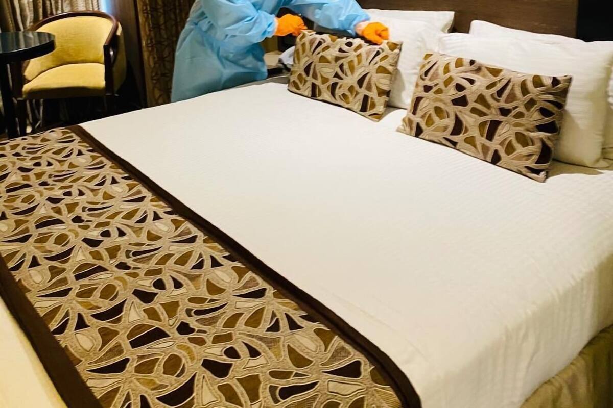 A hotel room with a neatly made bed, a patterned bedspread, and a decorative headboard.
