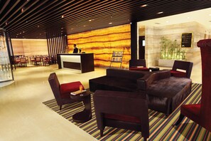 A modern lobby with a reception desk, seating area, and a decorative wall. - Hotel Vrisa (Jaipur)