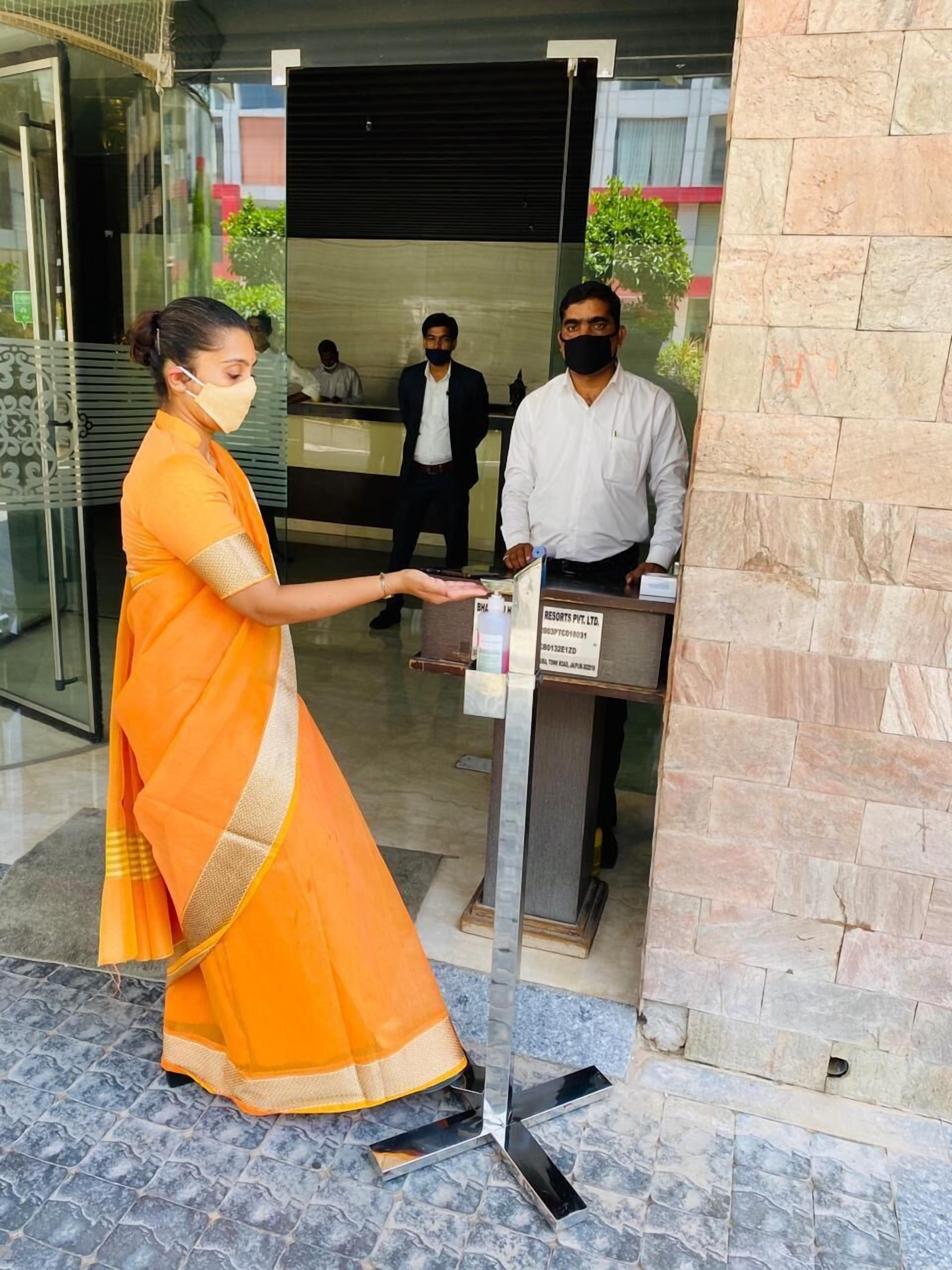Una mujer con un sari naranja entrega un documento a un hombre en la recepción de un hotel, con paredes de piedra y una entrada de cristal.