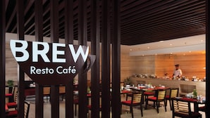 A restaurant interior with tables and chairs, a counter with a chef, and a sign reading "BREW Resto Café". - Hotel Vrisa (Jaipur)