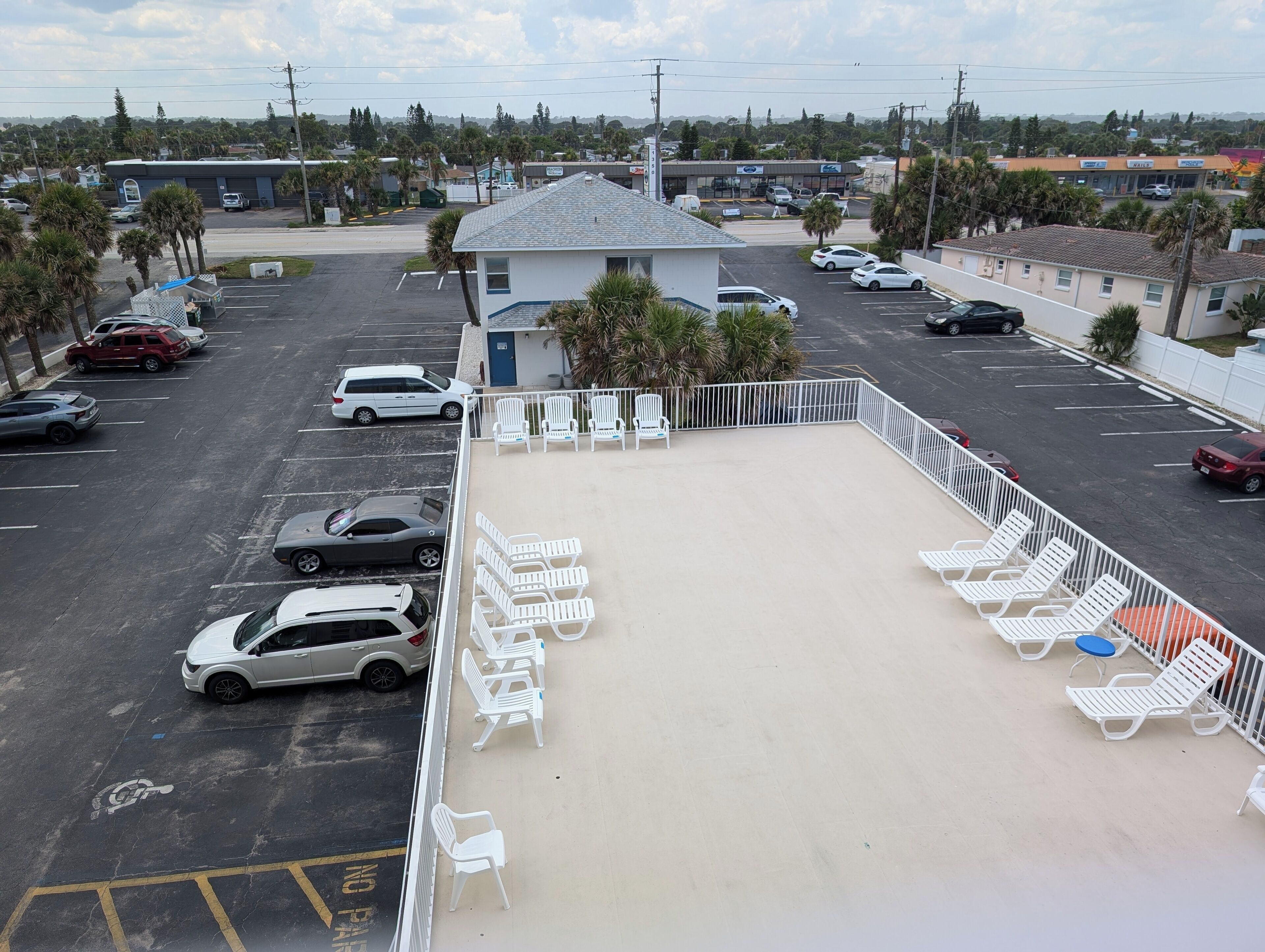 A parking lot with several cars, a small building, and a row of white lounge chairs.