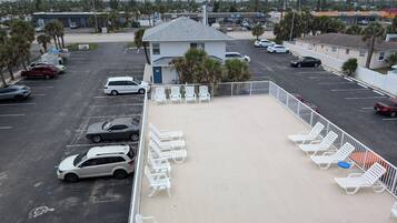 A parking lot with several cars, a small building, and a row of white lounge chairs.