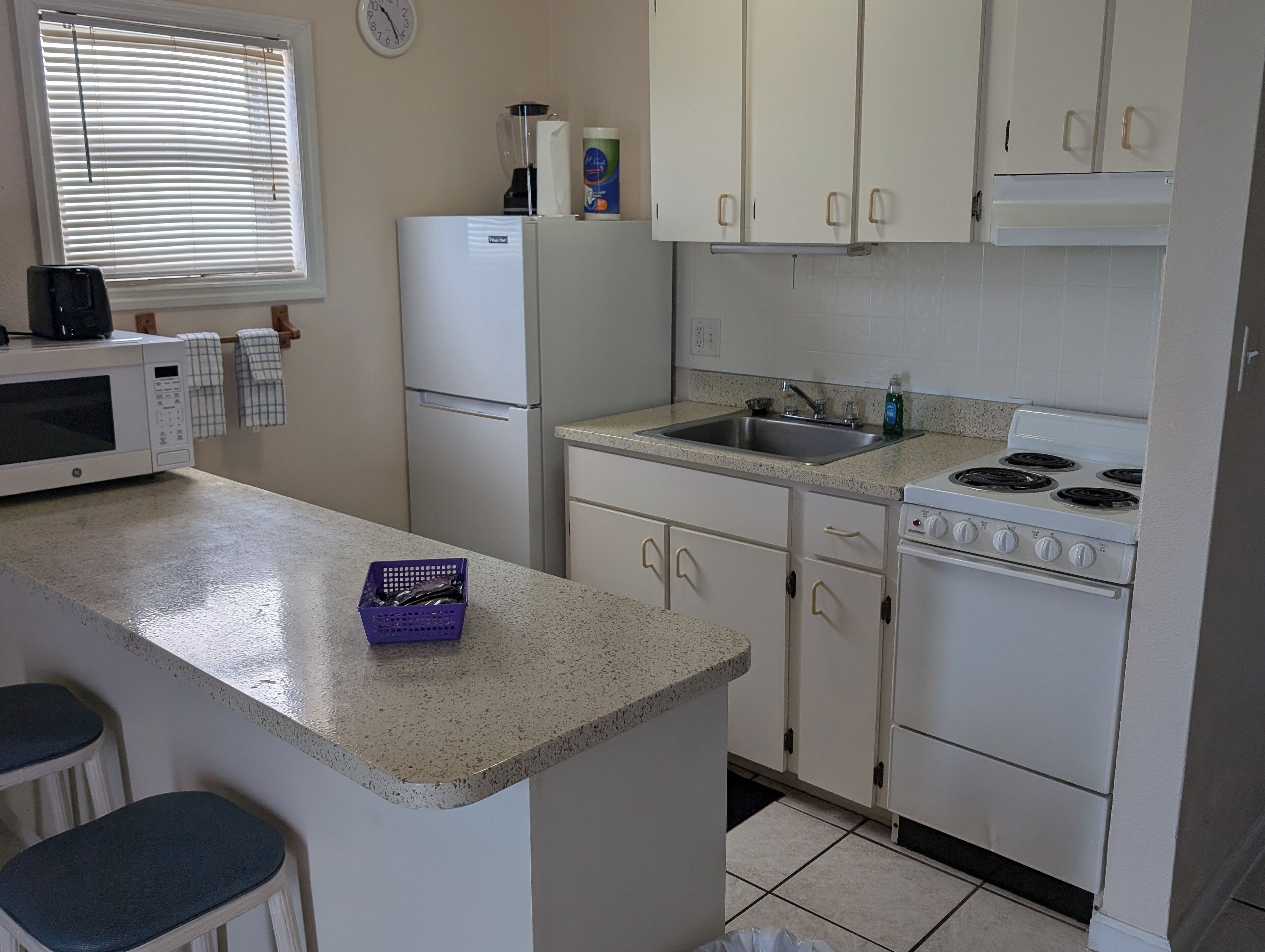 A compact kitchen with white cabinets, a microwave, a refrigerator, a sink, and a stove.