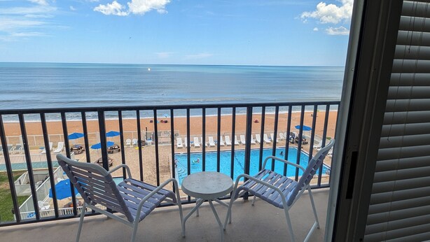 A balcony with a pool, chairs, and a view of the beach and ocean. - Traders Inn Beach Club (Ormond Beach)