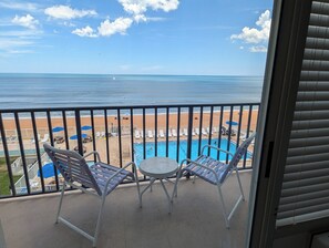 A balcony with a pool, chairs, and a view of the beach and ocean.