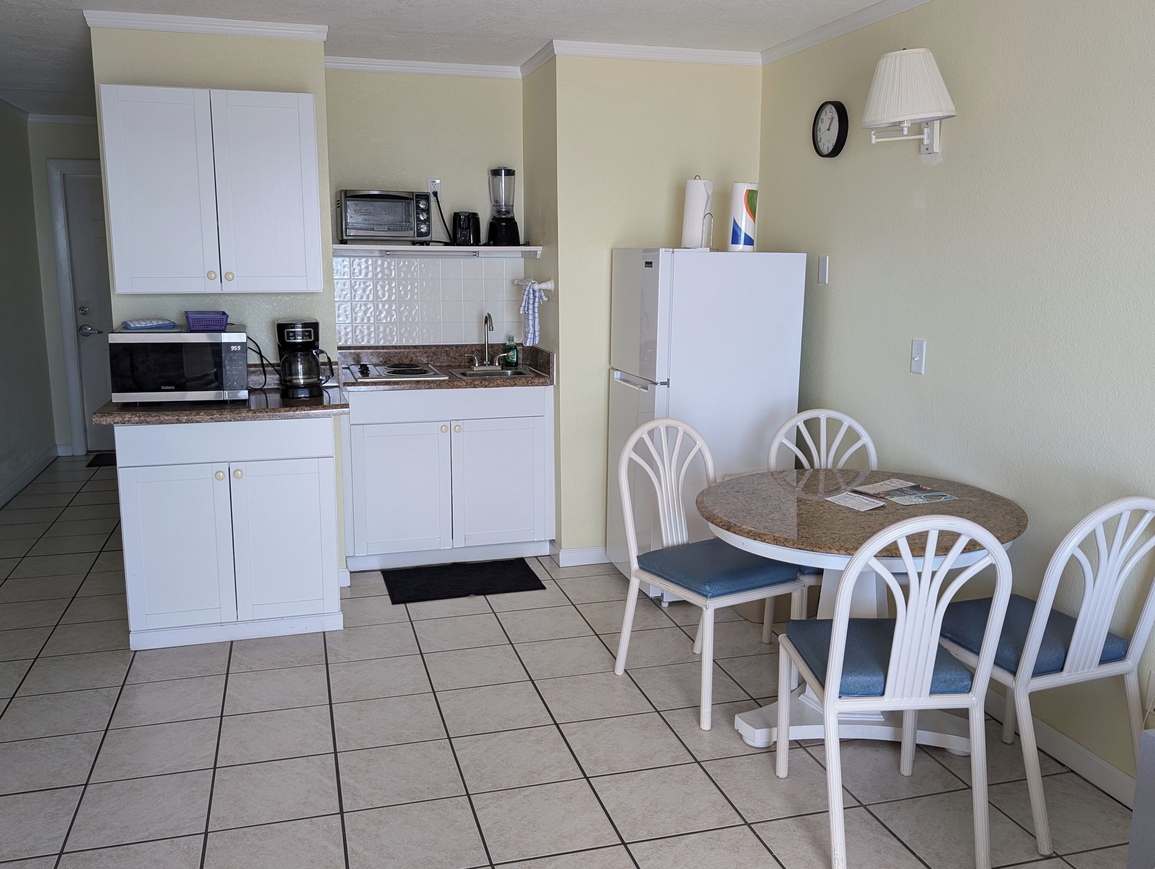 A compact kitchen with white cabinets, a microwave, a coffee maker, and a refrigerator. There is a small dining table with four chairs.