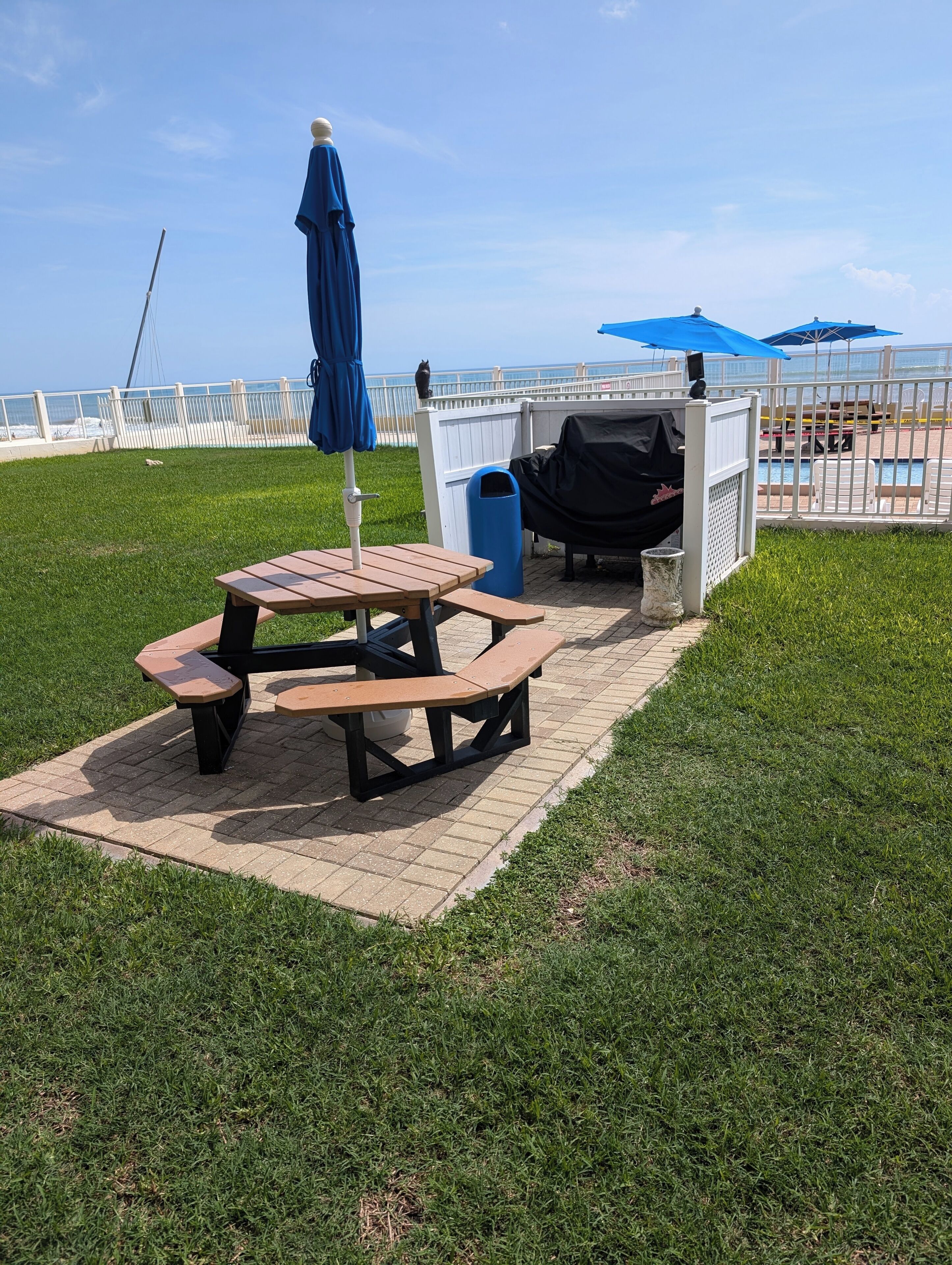 Une table de pique-nique avec des bancs, un barbecue et une poubelle, le tout installé dans un espace verdoyant avec vue sur la plage.