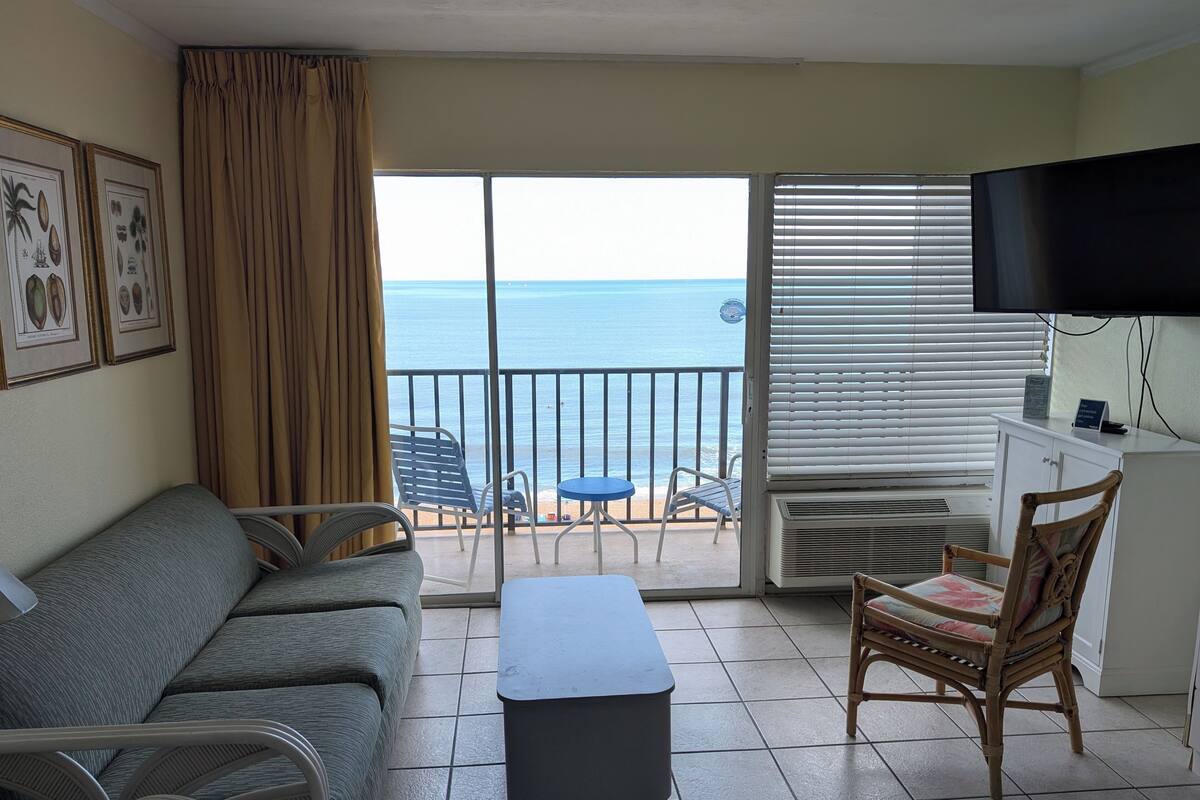Un balcón con vista al mar, un sofá, una silla, una mesa y un televisor.