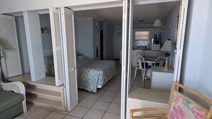 A compact room with a bed, a small desk, and a chair. - Traders Inn Beach Club (Ormond Beach)