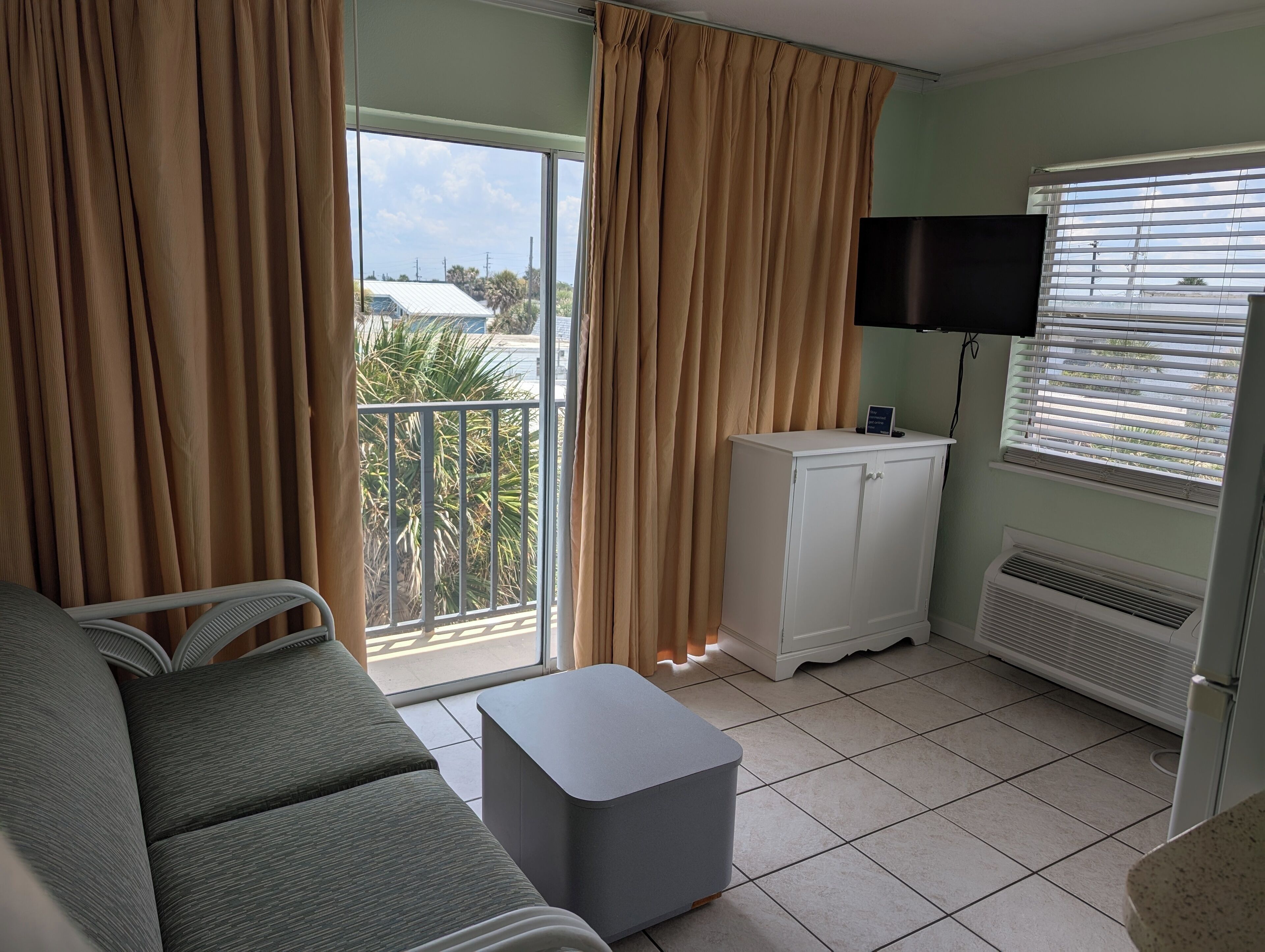A room with a sofa, a small table, a TV on a stand, a cabinet, and a window with blinds.