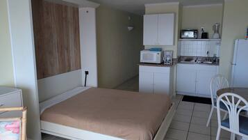 A compact room with a bed, kitchenette, and a small dining area.