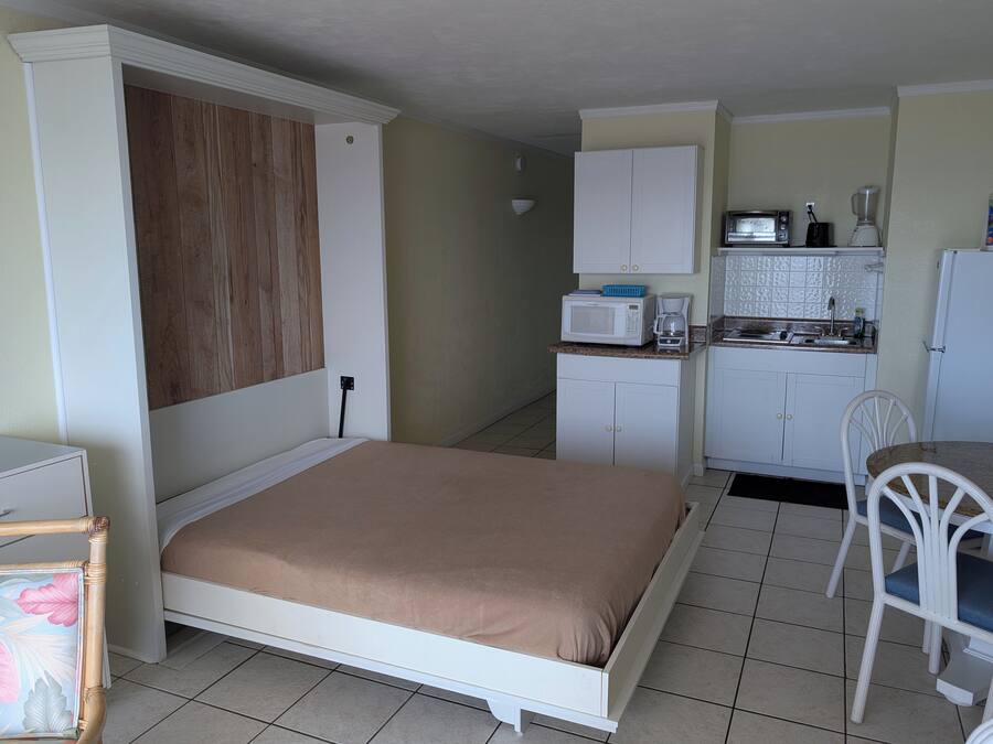 Quarto compacto com cama, cozinha compacta e pequena área de refeições.