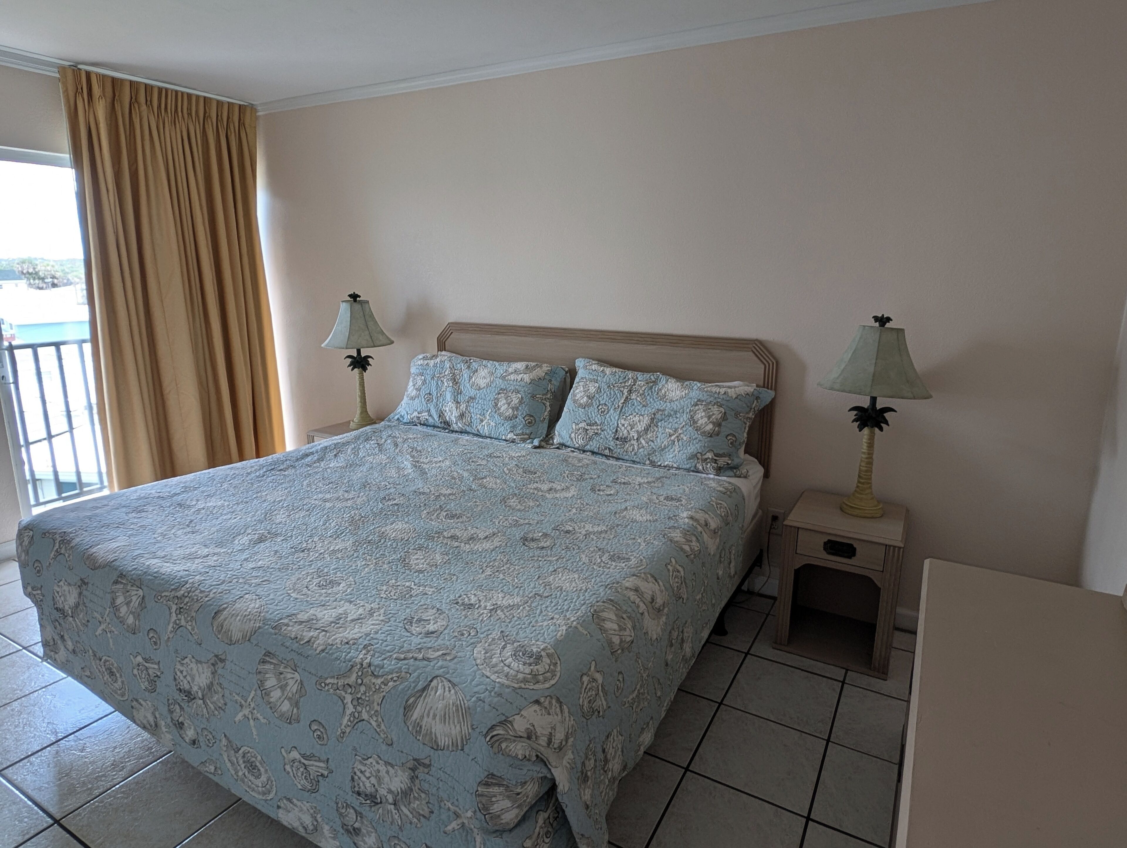 A bedroom with a bed, two bedside lamps, a nightstand, and a view of the outside through a window with curtains.
