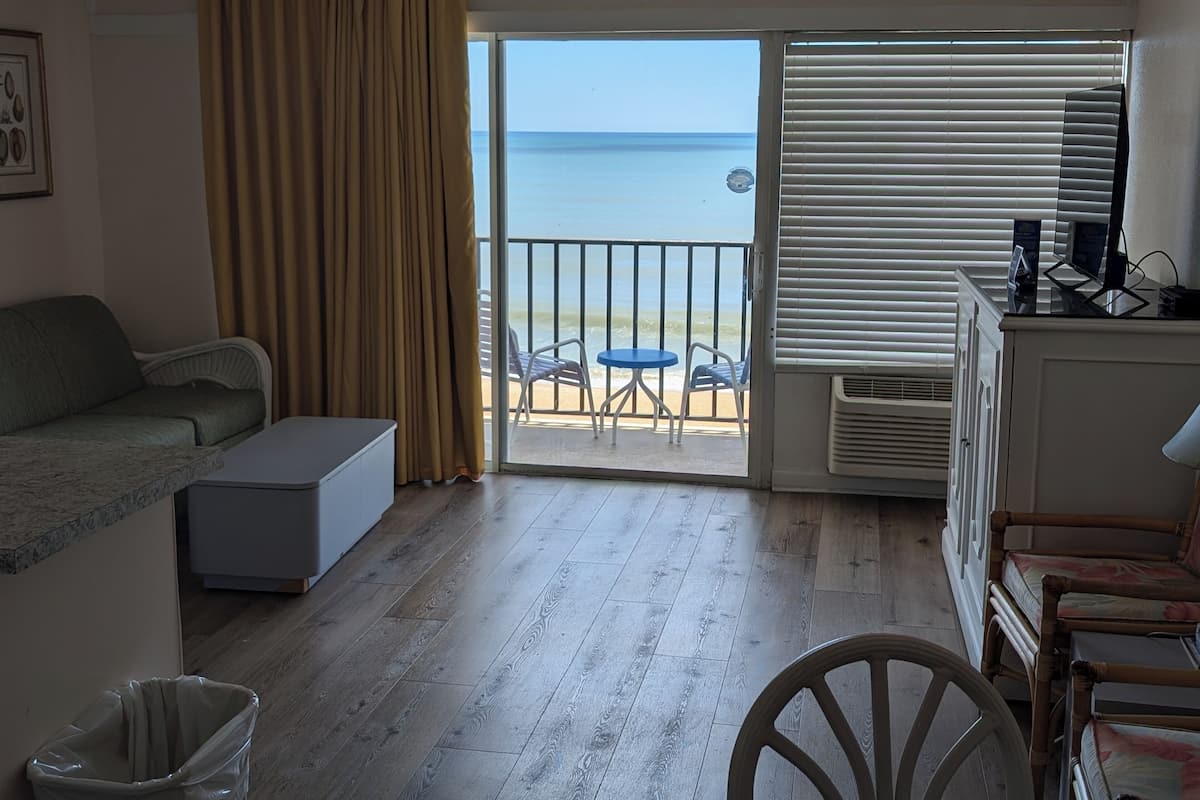 Una habitación con sofá, una mesita, un cubo de basura y vista a la playa a través de una puerta corredera.