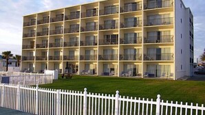 A multi-story hotel with balconies, a white fence, and a grassy lawn. - Traders Inn Beach Club (Ormond Beach)
