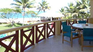 A balcony with a view of the beach, palm trees, and a table with chairs. - Agualina Kite Resort (Cabarete)
