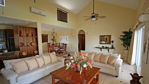 A spacious living room with a white sofa, a wooden coffee table with a floral centerpiece, and a ceiling fan. - Agualina Kite Resort (Cabarete)