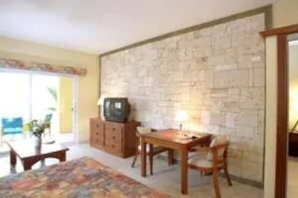 A room with a stone wall, a wooden table, and a television on a cabinet. - Agualina Kite Resort (Cabarete)