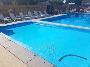 Relax by the pool surrounded by lounge chairs and a wooden fence.