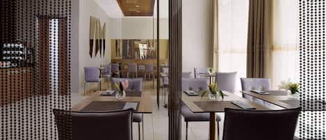 A modern dining area with multiple tables and chairs, a central decorative column, and a view into a kitchen area.