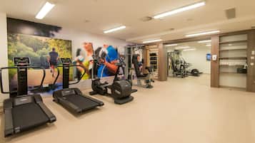 Une salle de sport équipée de tapis de course, d’appareils de musculation et ornée d’une grande fresque représentant des coureurs.