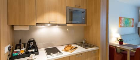 Una cocina compacta con armarios de madera, microondas, cafetera y un pequeño comedor con una silla y una mesa.