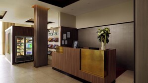A reception area with a wooden reception desk, a refrigerator stocked with beverages, and a wall-mounted display of books and magazines.