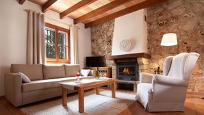 A cozy living room with a stone fireplace, a sofa, a chair, and a television. - Agroturismo Son Ginebró (Inca)