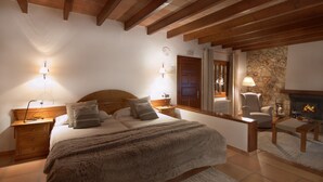 A bedroom with a wooden ceiling, a fireplace, a bed with a blanket, bedside lamps, and a nightstand. - Agroturismo Son Ginebró (Inca)