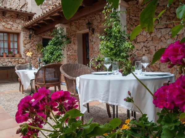 An outdoor patio with stone walls, wicker furniture, and tables set for dining. - Agroturismo Son Ginebró (Inca)
