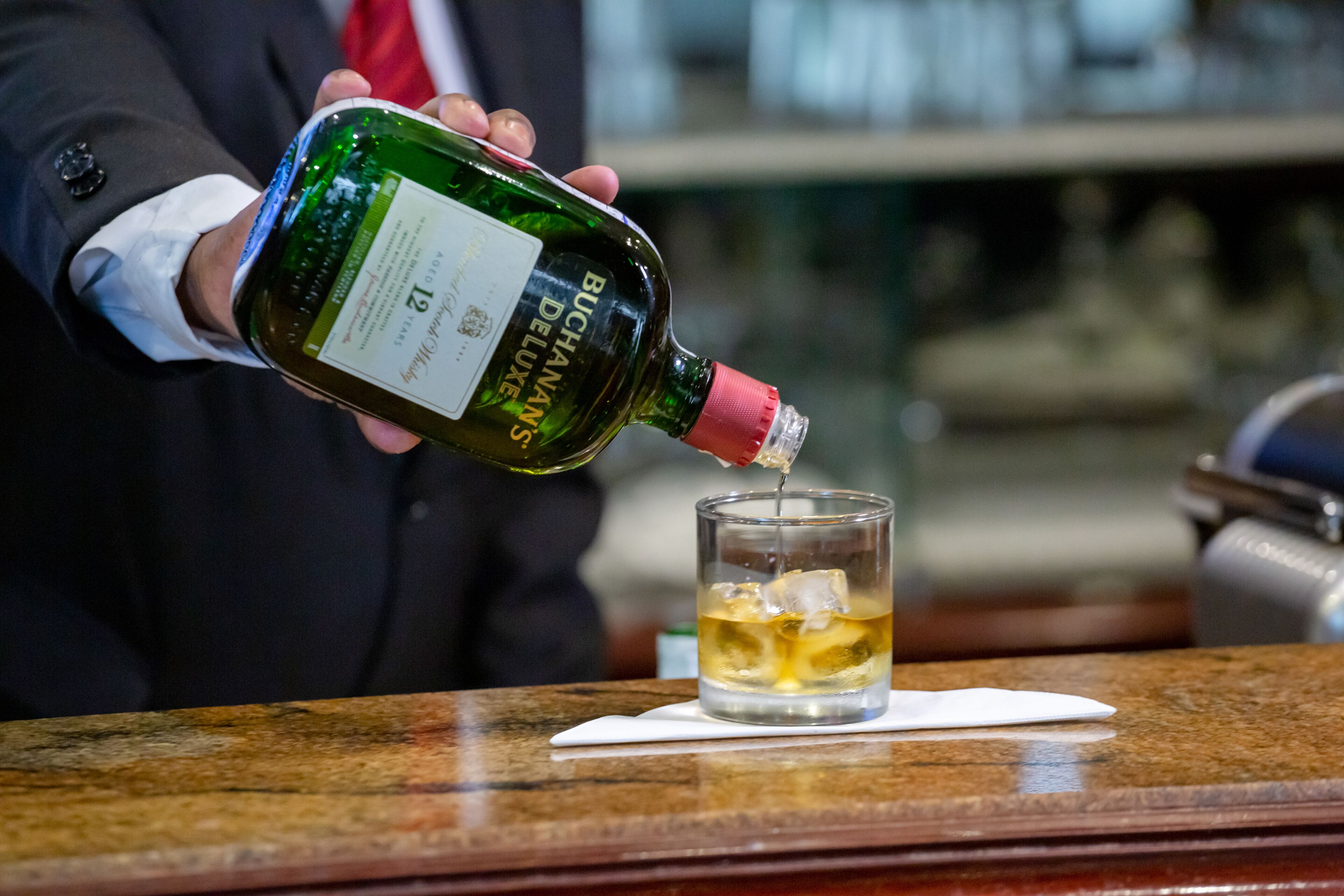 A person pouring a bottle of wine into a glass on a bar counter.