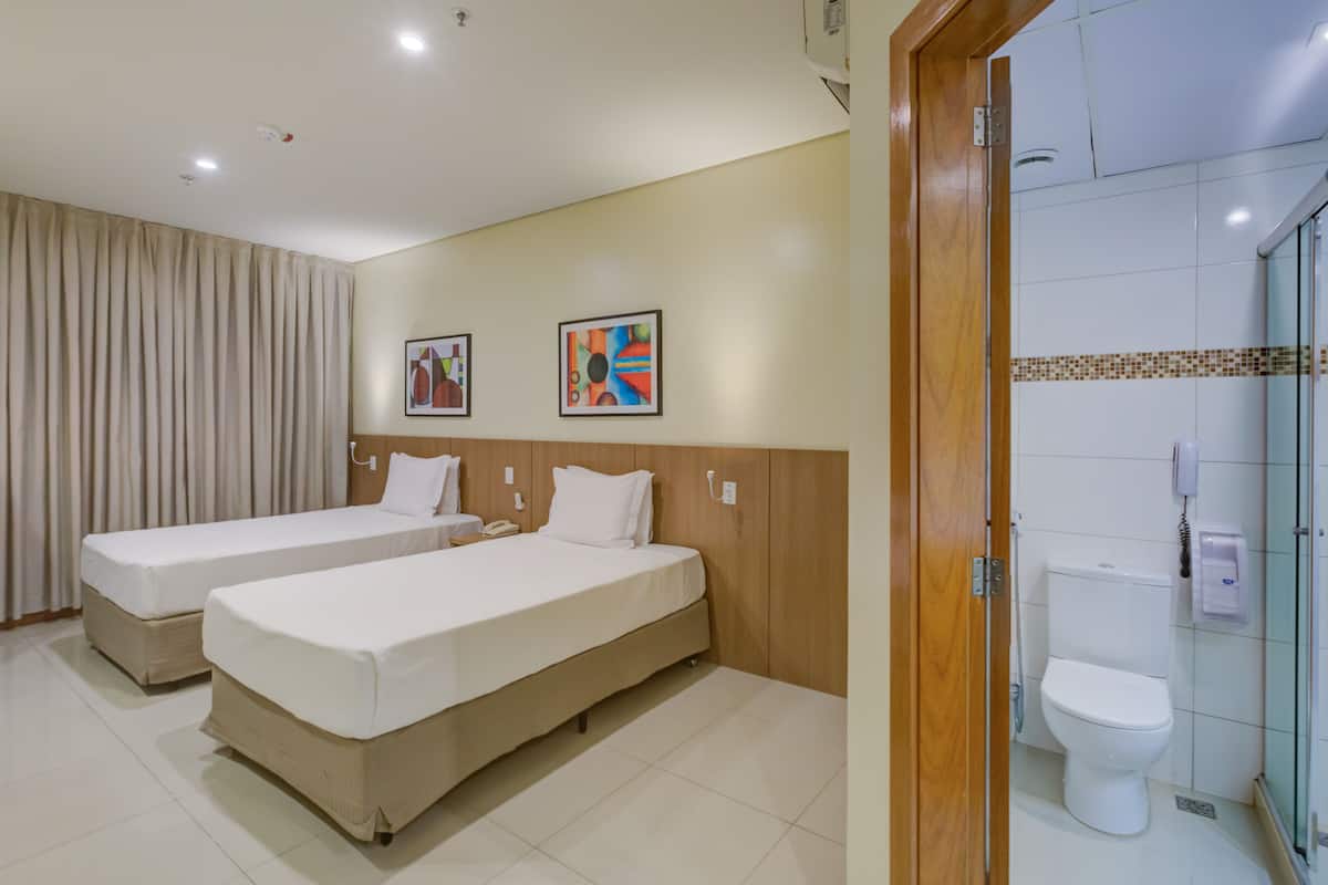 Une chambre d’hôtel avec deux lits, une salle de bain avec des toilettes et une douche, et deux tableaux encadrés au mur.